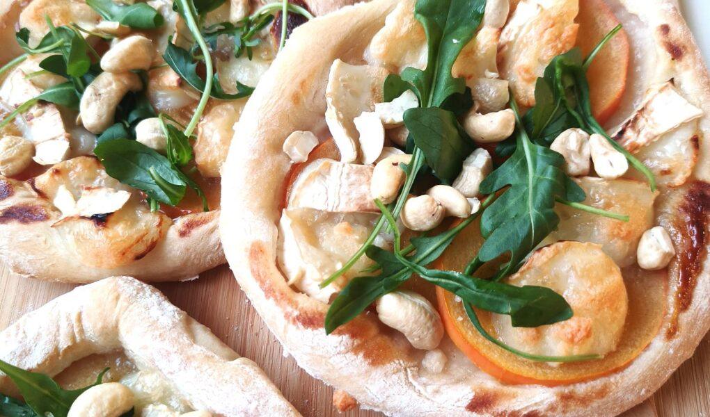 Pieniä pizzoja, joissa täytteenä vuohenjuustoa, persimonin viipaleita, rucolaa ja cashewpähkinöitä