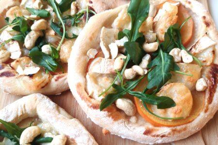Pieniä pizzoja, joissa täytteenä vuohenjuustoa, persimonin viipaleita, rucolaa ja cashewpähkinöitä